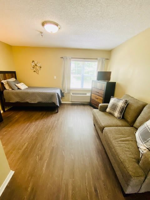 A cozy bedroom with a bed, sofa, and wooden flooring.