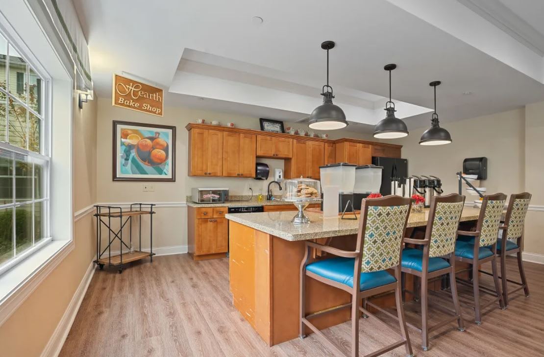 A modern kitchen with an island and wooden cabinets, featuring pendant lights and bar stools.