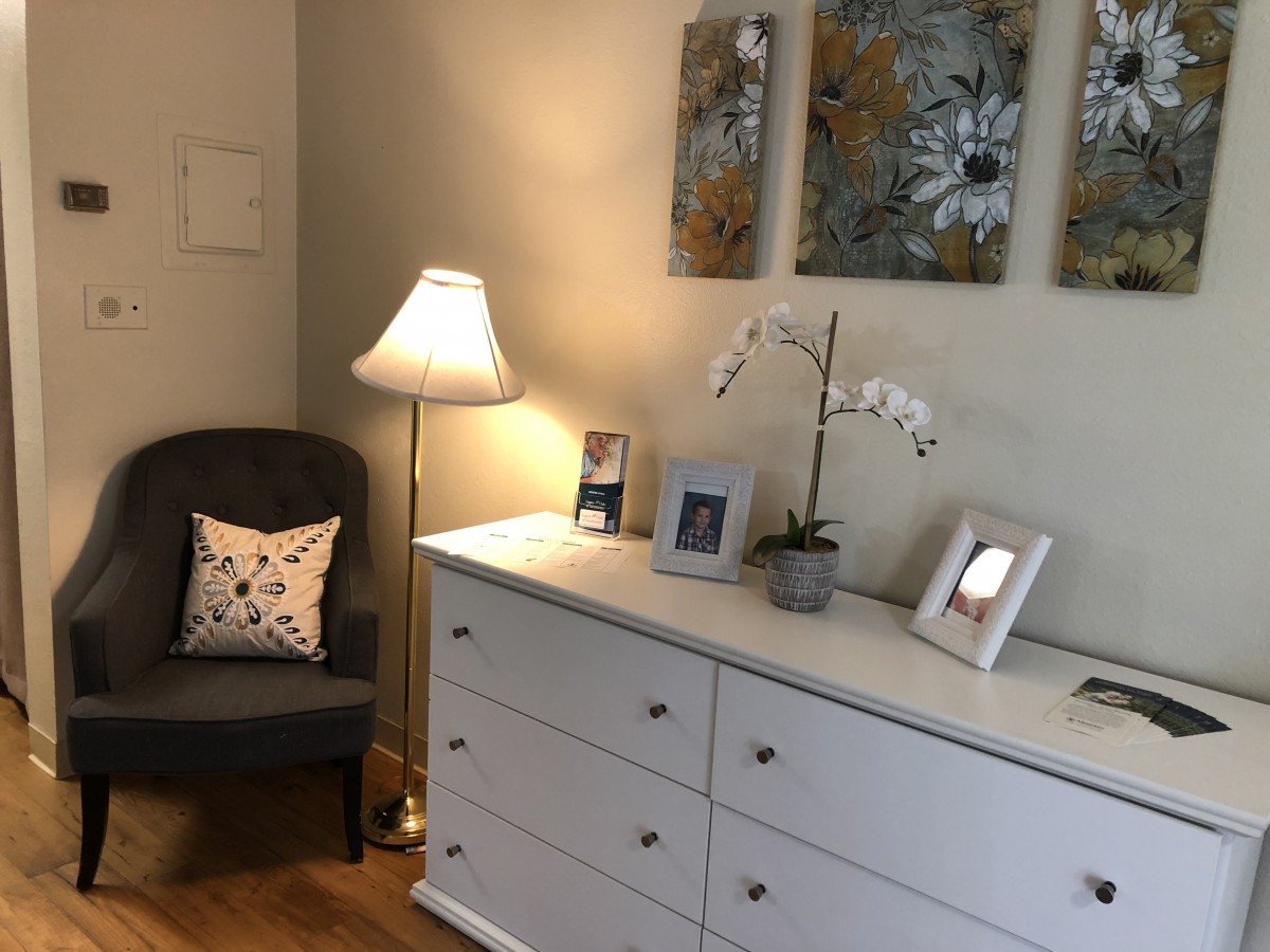 A cozy corner featuring a white dresser, upholstered chair, standing lamp, and decorative elements.