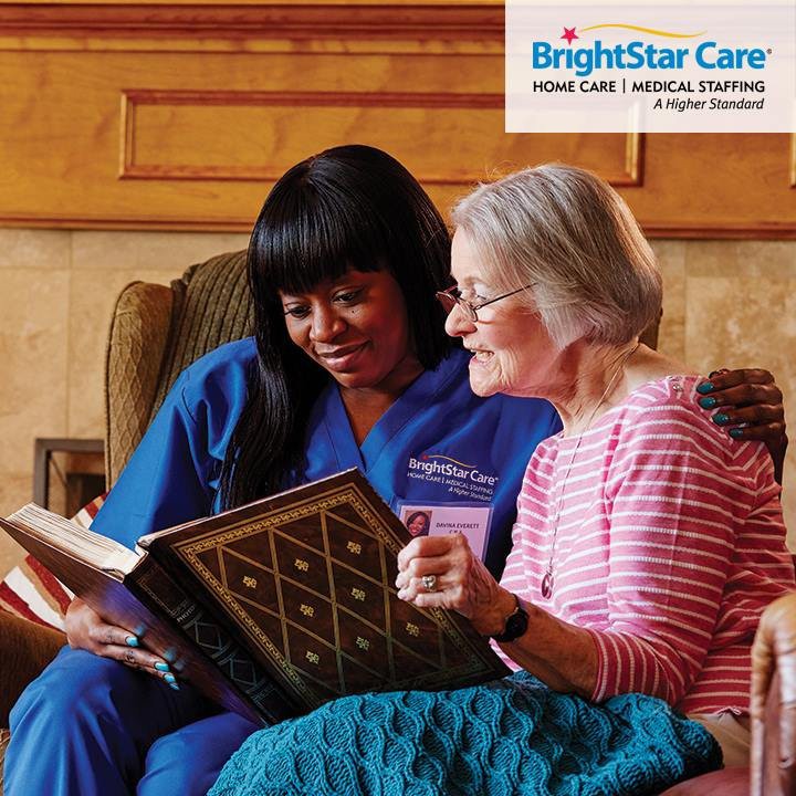 A caregiver and an elderly woman enjoy reading a book together, highlighting companionship in home care.