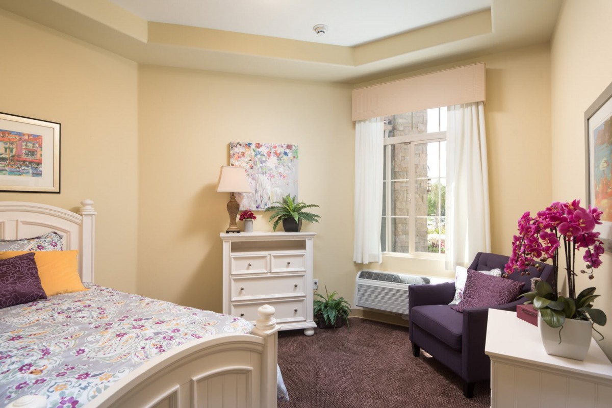 A cozy bedroom with soft lighting, featuring a comfortable chair by the window and tasteful decor.