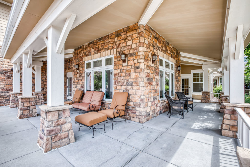 A spacious outdoor patio with stone walls, featuring comfortable seating and a table under a covered area.