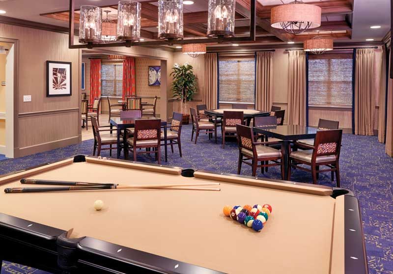 A cozy game room featuring a pool table and seating area, illuminated by stylish overhead lighting.