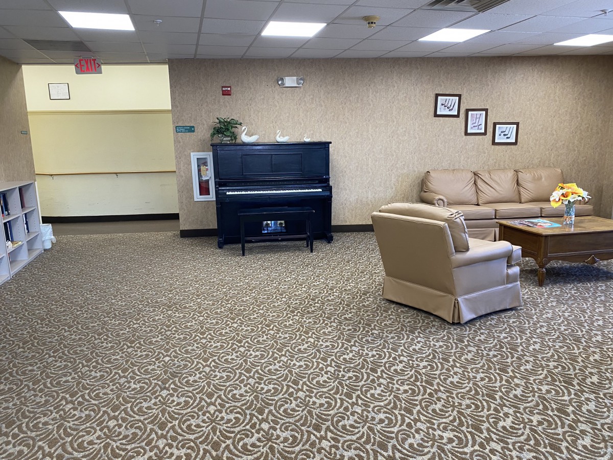 A lobby area featuring a piano, sofas, and chairs on a patterned carpet.