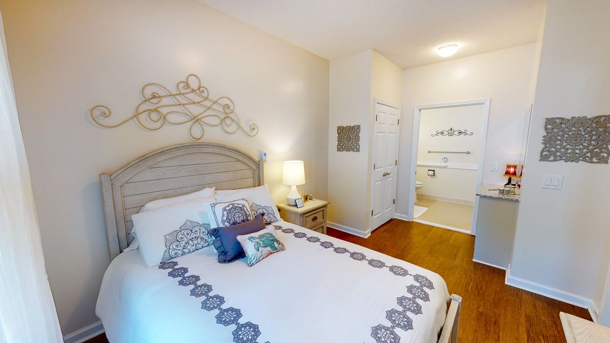 A cozy and modern bedroom featuring a neatly made bed with decorative pillows, a nightstand with a lamp, and an elegant wall decor.