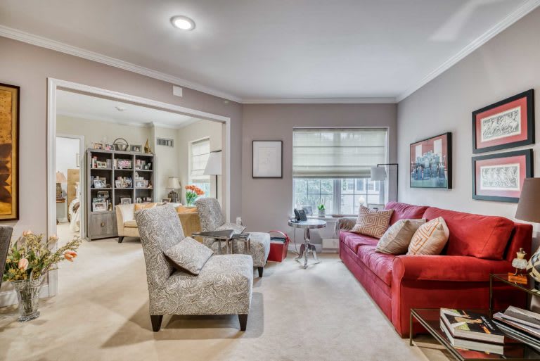 A cozy living room featuring a red sofa, patterned chairs, and a bookshelf in the adjacent area.