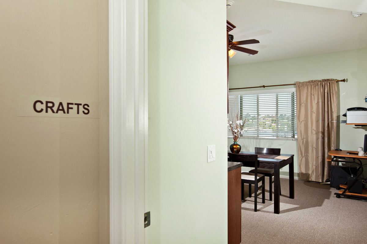 A view of a crafts room with a dining table and ceiling fan, seen through an open doorway.