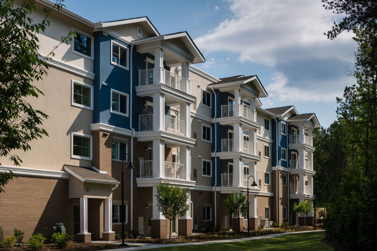 A modern multi-story apartment building with a mix of beige and blue exteriors under a partly cloudy sky.