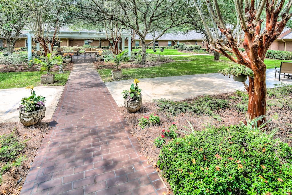 A scenic garden with a pathway, surrounded by lush greenery and benches.