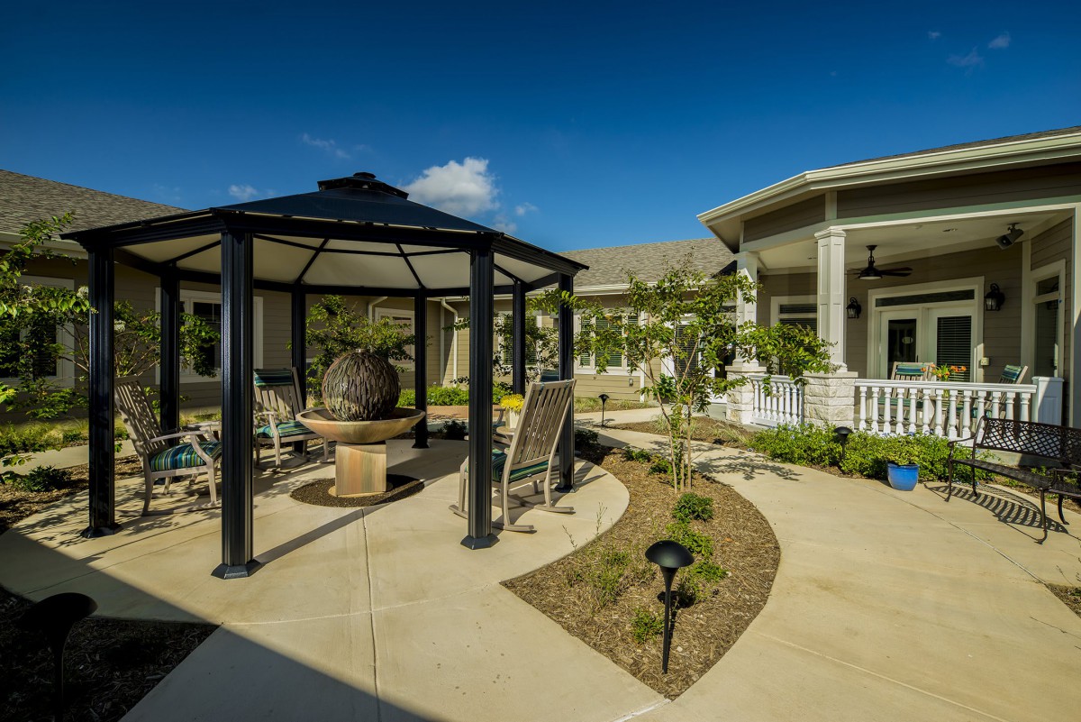A well-maintained garden featuring a gazebo and a modern building under a clear blue sky.