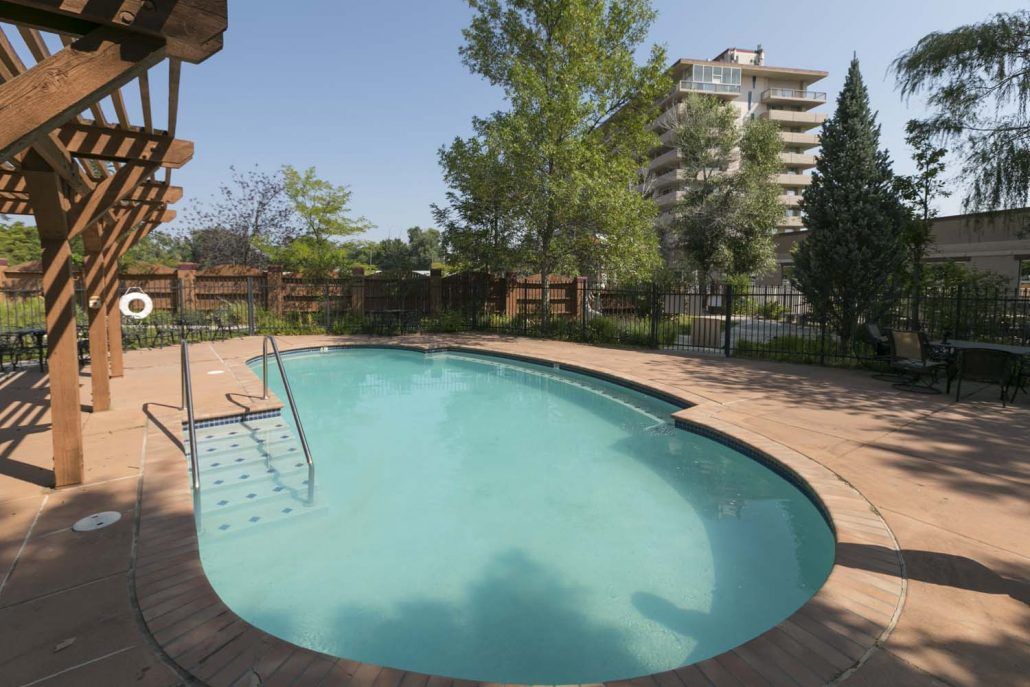 A tranquil outdoor swimming pool surrounded by trees and a nearby building.