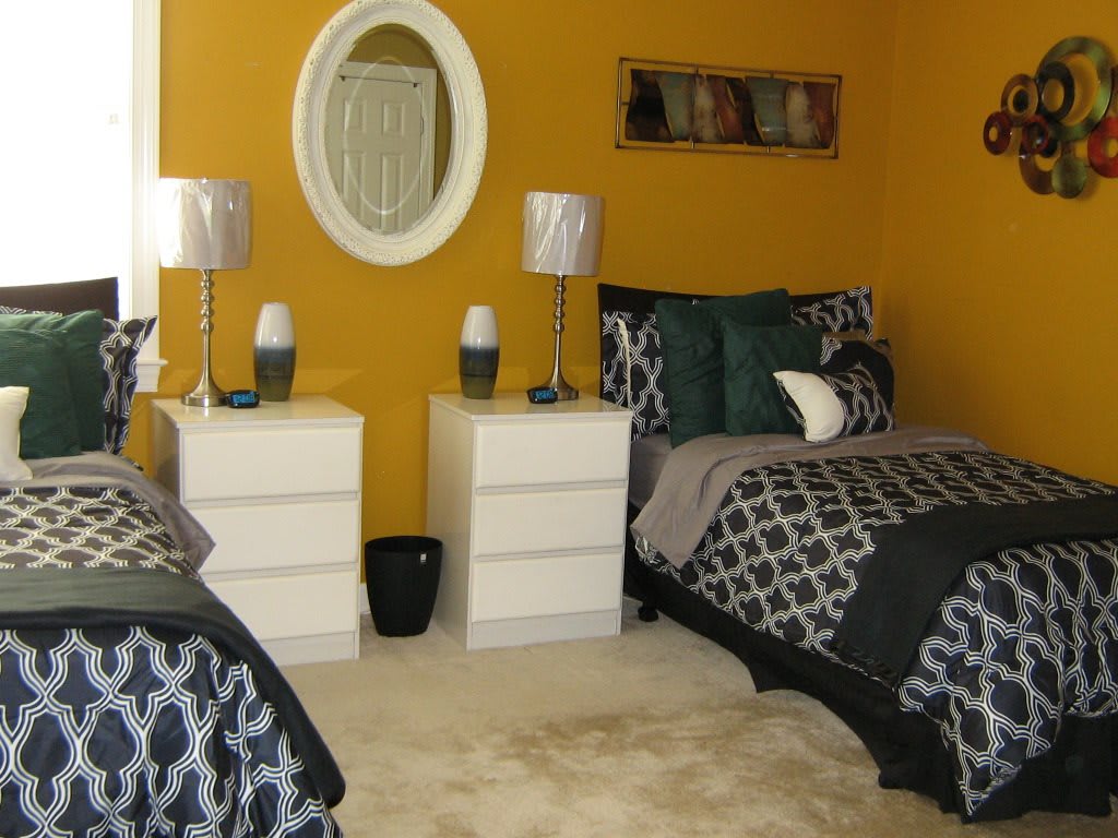 A cozy bedroom with twin beds, featuring a vibrant yellow wall and white furniture.