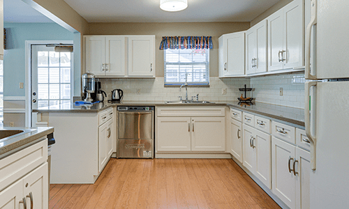 A modern kitchen with white cabinets, a stainless steel dishwasher, and wooden flooring.