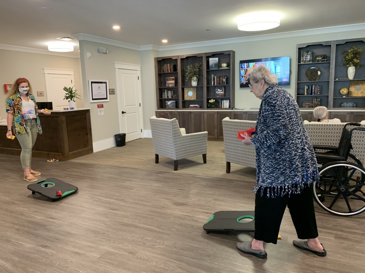An elderly woman enjoys a game of bean bag toss in a comfortable living room setting.