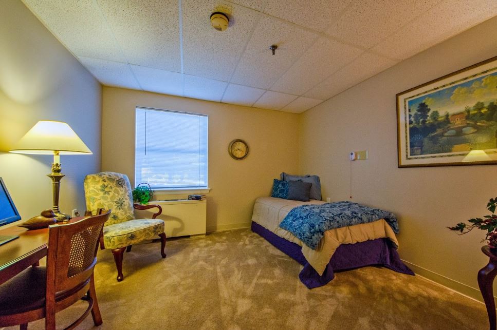 A cozy bedroom featuring a single bed, an armchair, and a window allowing natural light to fill the space.