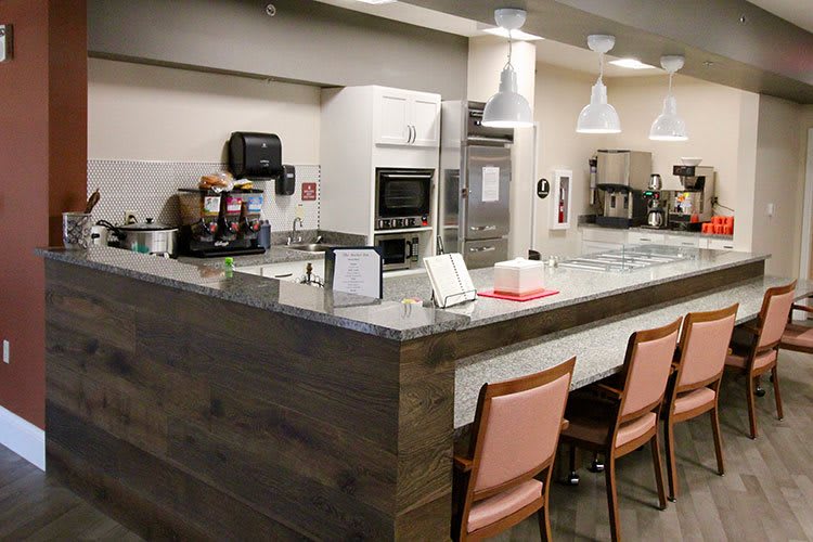 A modern kitchen with a counter and chairs, featuring various appliances and lighting.