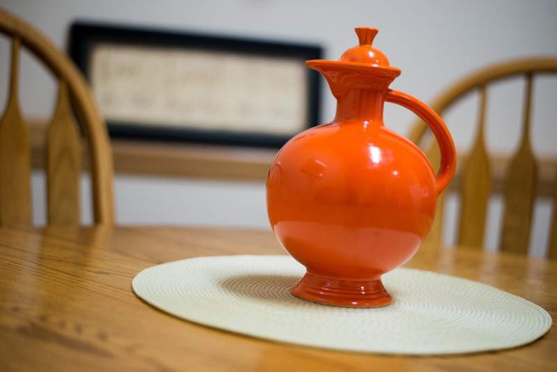 A brightly colored orange ceramic jug sits on a table as a decorative piece.