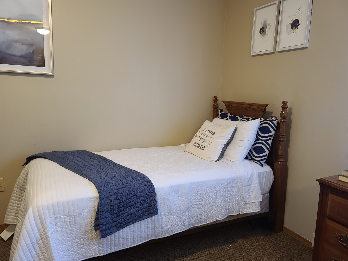 A neatly arranged single bed in a minimalist bedroom with wall art.