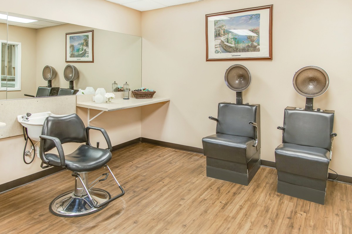 A cozy salon interior featuring styling chairs and hair dryers with a large mirror and wooden flooring.