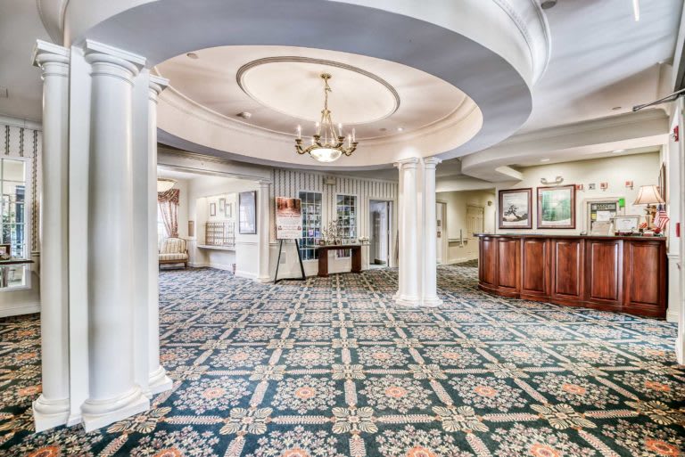 A spacious hotel lobby featuring ornate columns, a chandelier, and patterned carpeting.