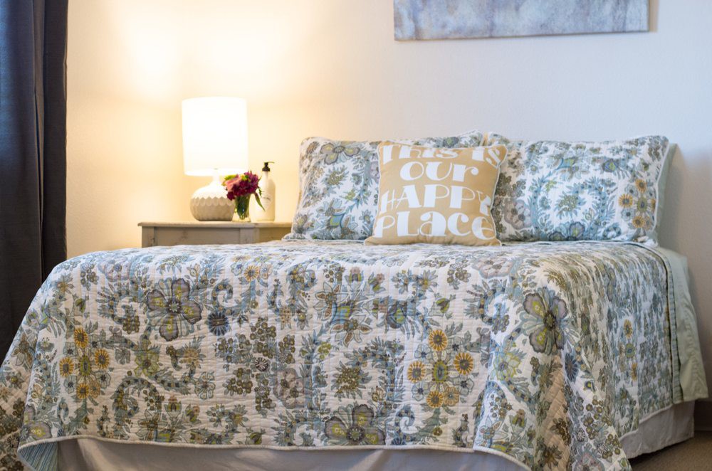 A cozy bedroom setup with patterned bedding and a softly lit lamp on the nightstand.