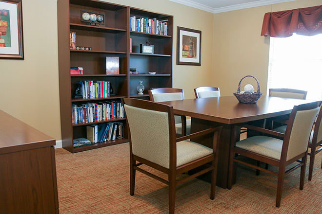 A cozy meeting room with a wooden table, chairs, and a filled bookshelf.
