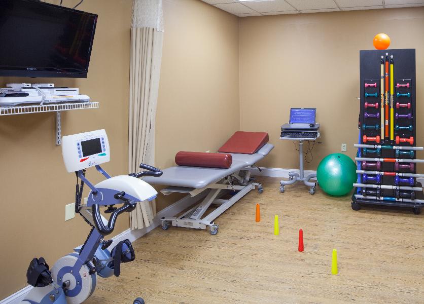 A well-equipped physiotherapy and rehabilitation treatment room with an exercise bike, therapy bed, and various workout equipment.