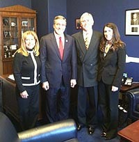 A group of four people in formal attire standing together in an office setting.