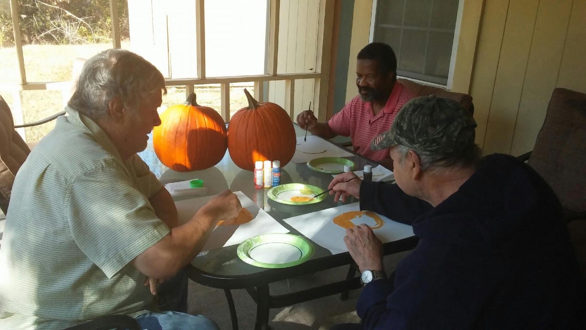 A group of people engaging in painting activities with pumpkins at an outdoor table.