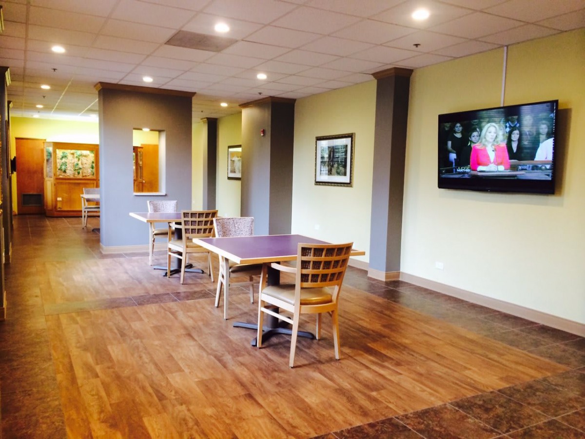 A modern lounge area with wooden flooring, tables and chairs, adorned by a wall-mounted television.