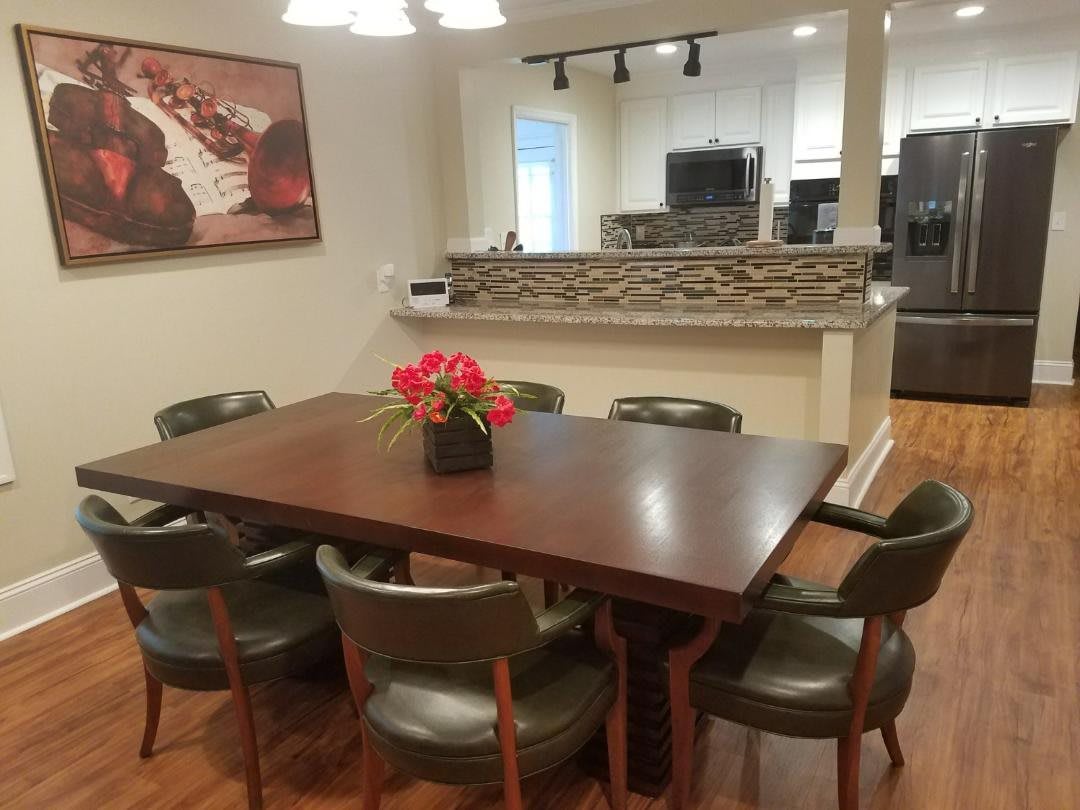 A dining area with a wooden table, surrounding chairs, and a flower centerpiece.