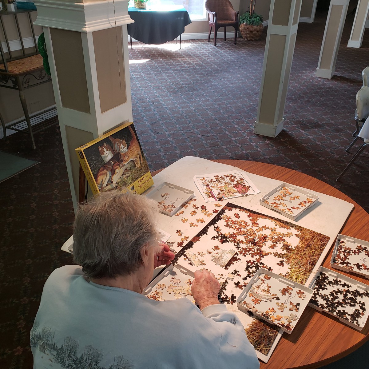 An elderly person working on a jigsaw puzzle at a table indoors.