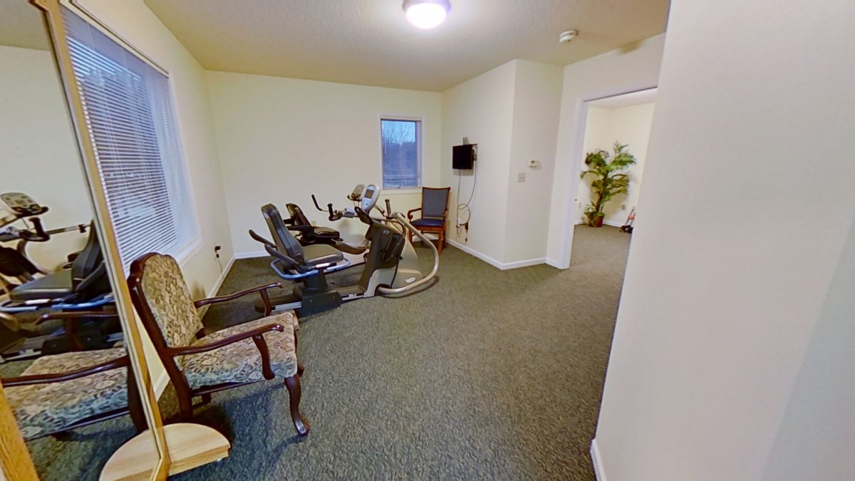 A small exercise room with fitness equipment, seating, and a television.