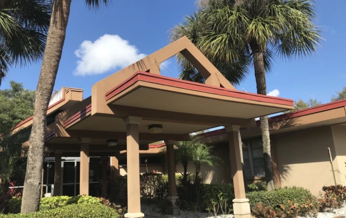 A building entrance with a modern architectural design, surrounded by palm trees under a clear blue sky.