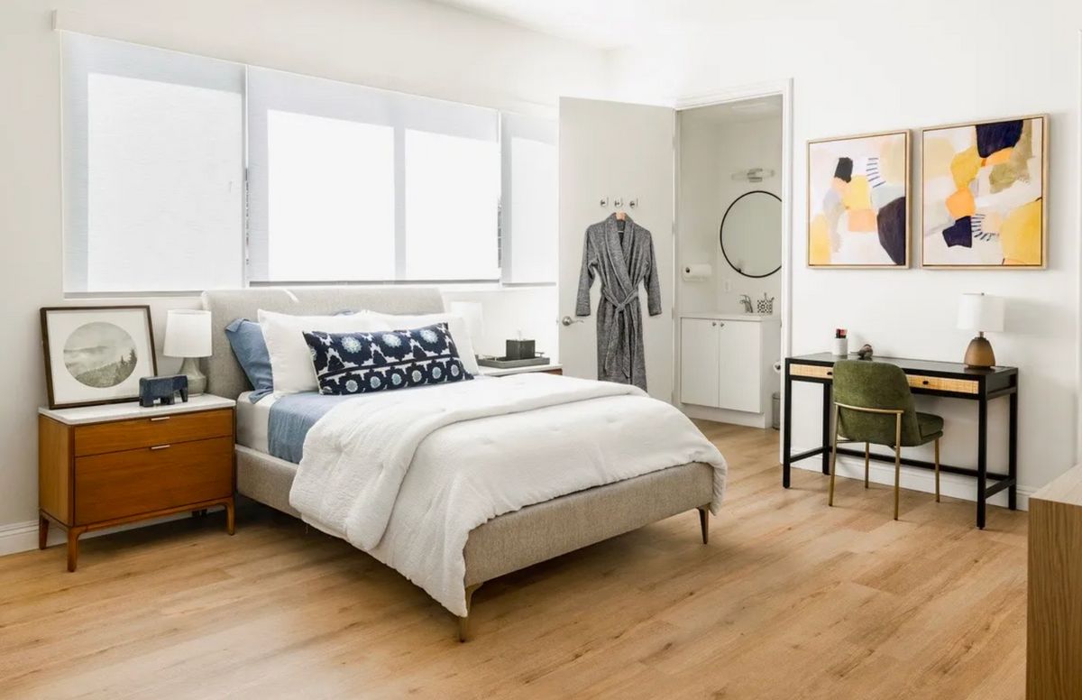 A modern and cozy bedroom with natural light streaming through large windows, featuring stylish furniture and decor.