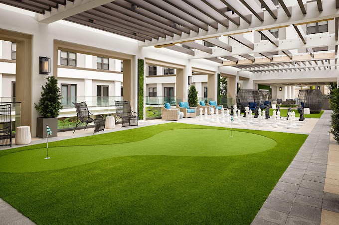 A modern outdoor patio with artificial turf and comfortable seating under a pergola.