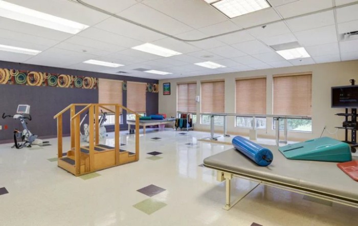 A spacious physical therapy room with exercise equipment and parallel bars for rehabilitation exercises.