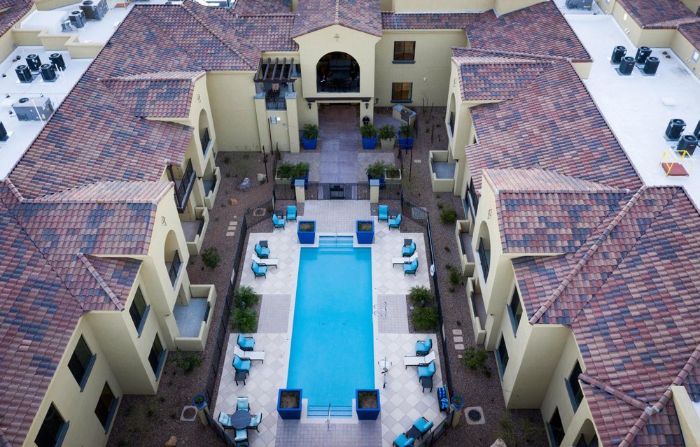 Aerial view of a luxury apartment complex featuring a central swimming pool surrounded by lounge chairs.