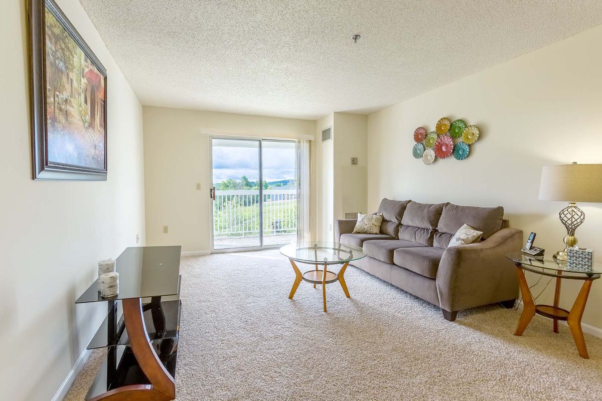 A bright and cozy living room with a sofa and coffee table, featuring patterned wall decor and a view through large sliding doors.