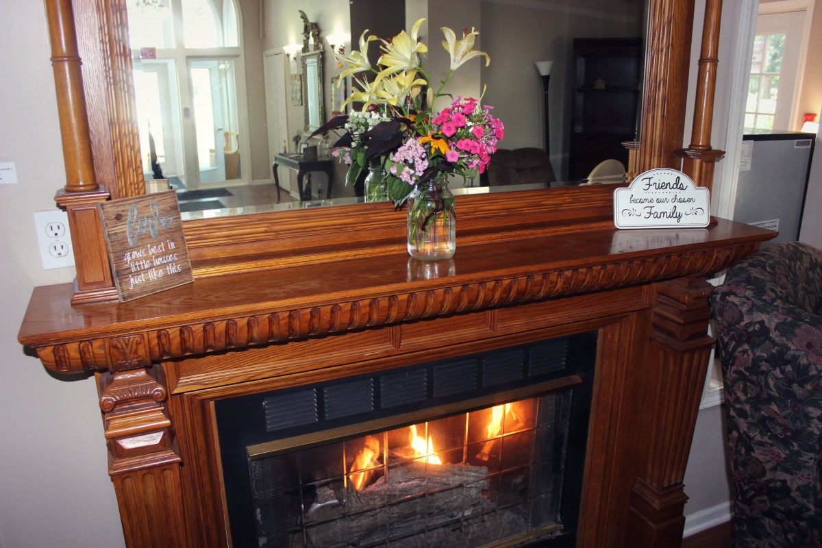 A cozy fireplace with a wooden mantel adorned with a vase of colorful flowers.