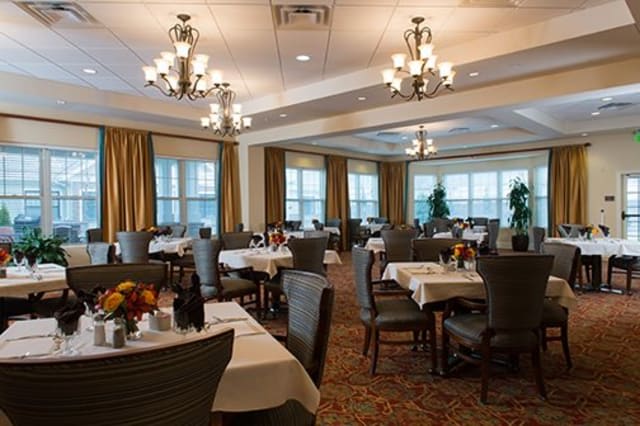 An elegant restaurant dining room with neatly arranged tables and chairs, illuminated by chandeliers.