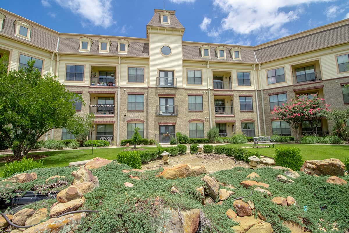 A beautiful apartment complex with a well-maintained garden and clear blue sky.