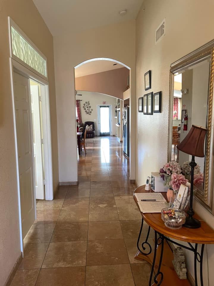 A well-decorated hallway with a mirror, lamp, and table, leading to rooms through an arched doorway.