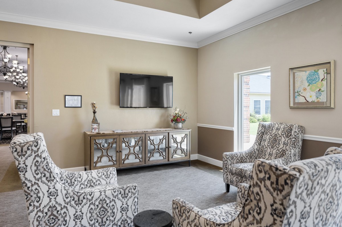 A stylish living room with patterned armchairs, a mirrored cabinet, and a mounted television.