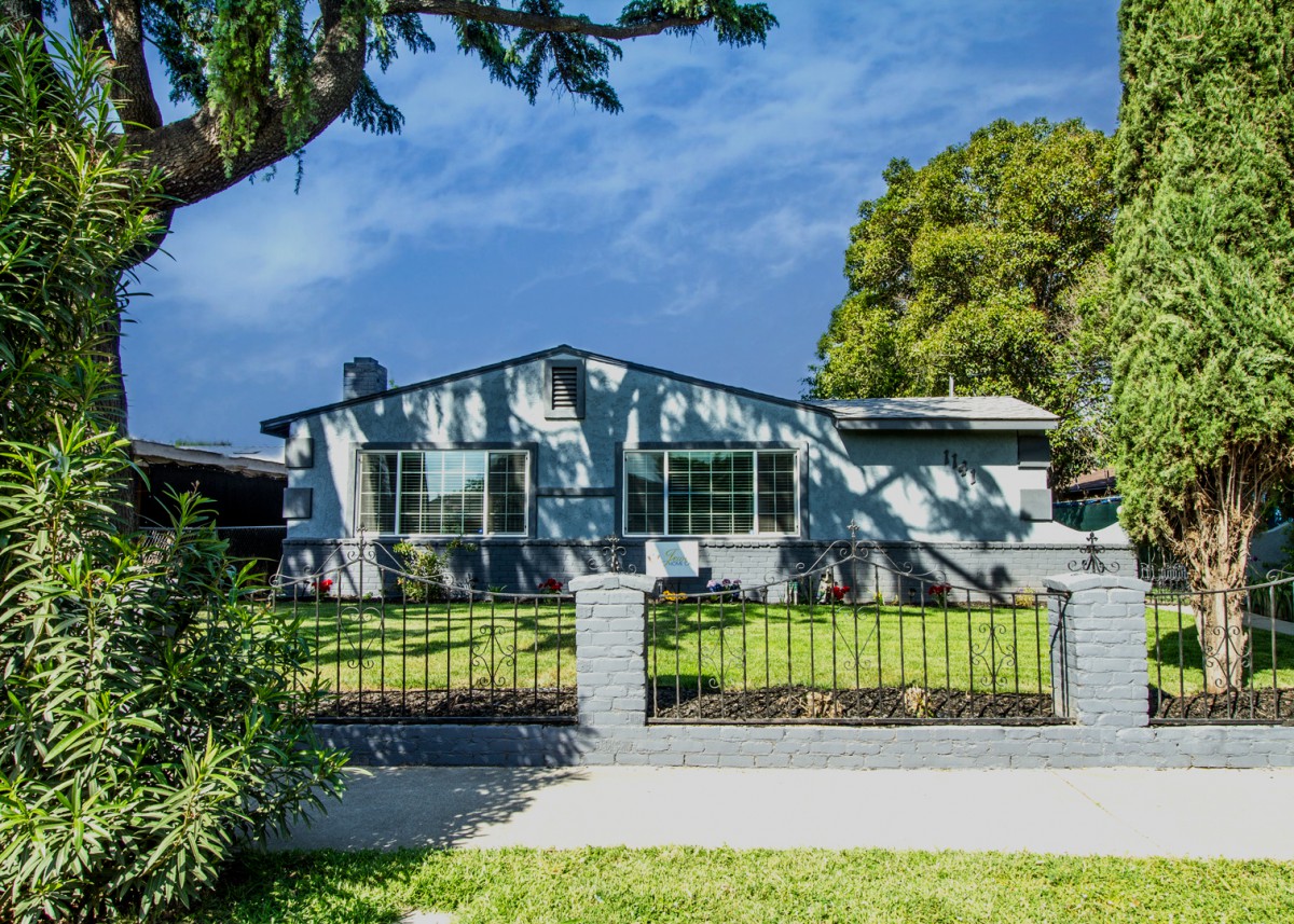 A suburban house with a spacious yard and a metal fence under a clear blue sky.