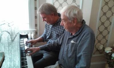 Two men playing a duet on the piano indoors.