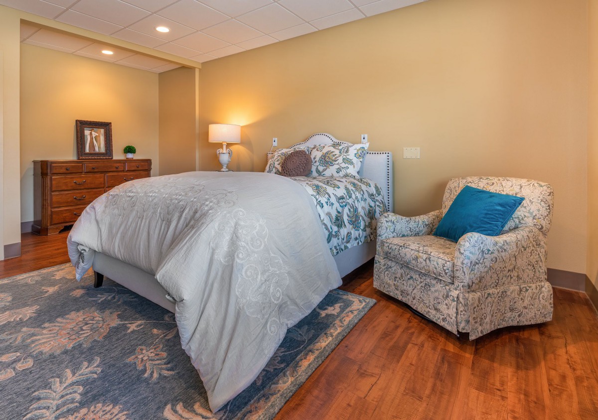 A cozy bedroom with a large bed, an armchair, and soft lighting.