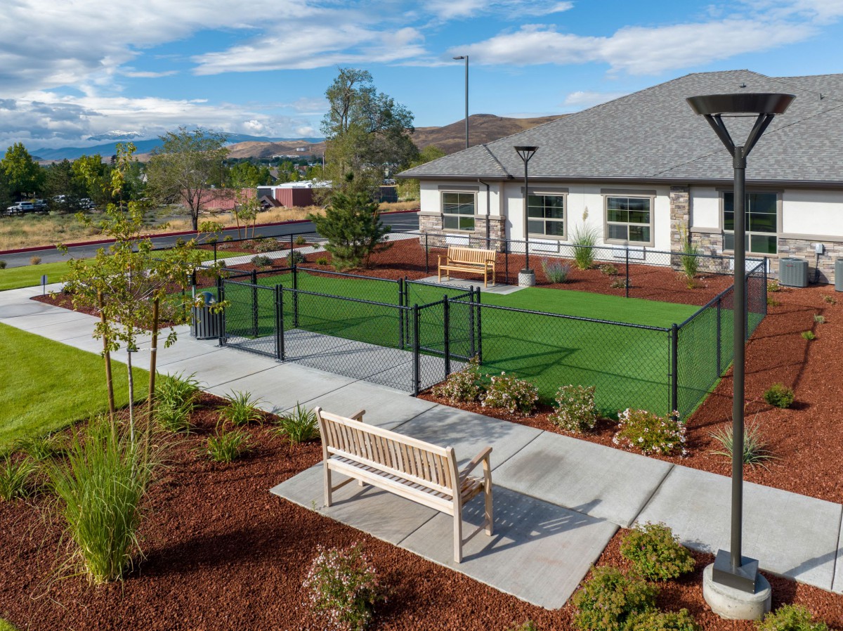 A landscaped outdoor area with benches, a fenced section of artificial turf, and a building in the background.