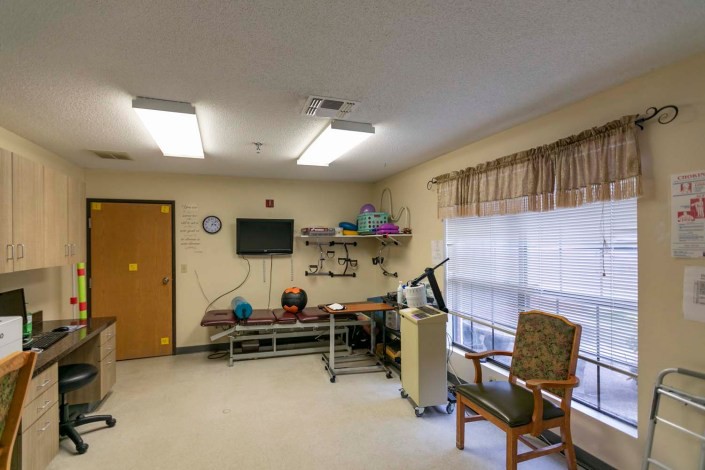 A rehabilitation therapy room equipped with medical apparatus, a window with curtains, and seating.