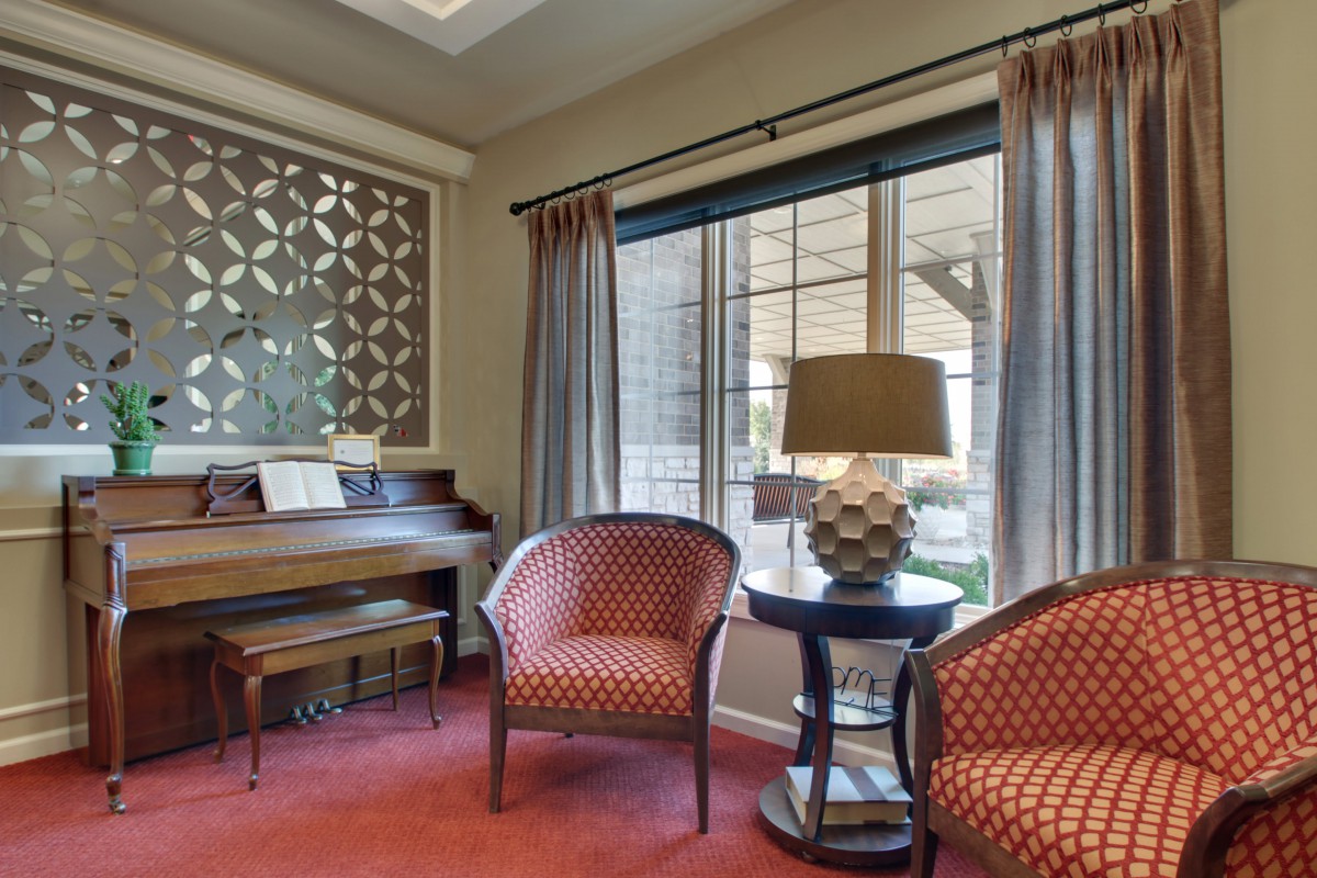A cozy living room featuring a piano, two armchairs, and a stylish lamp by the window.